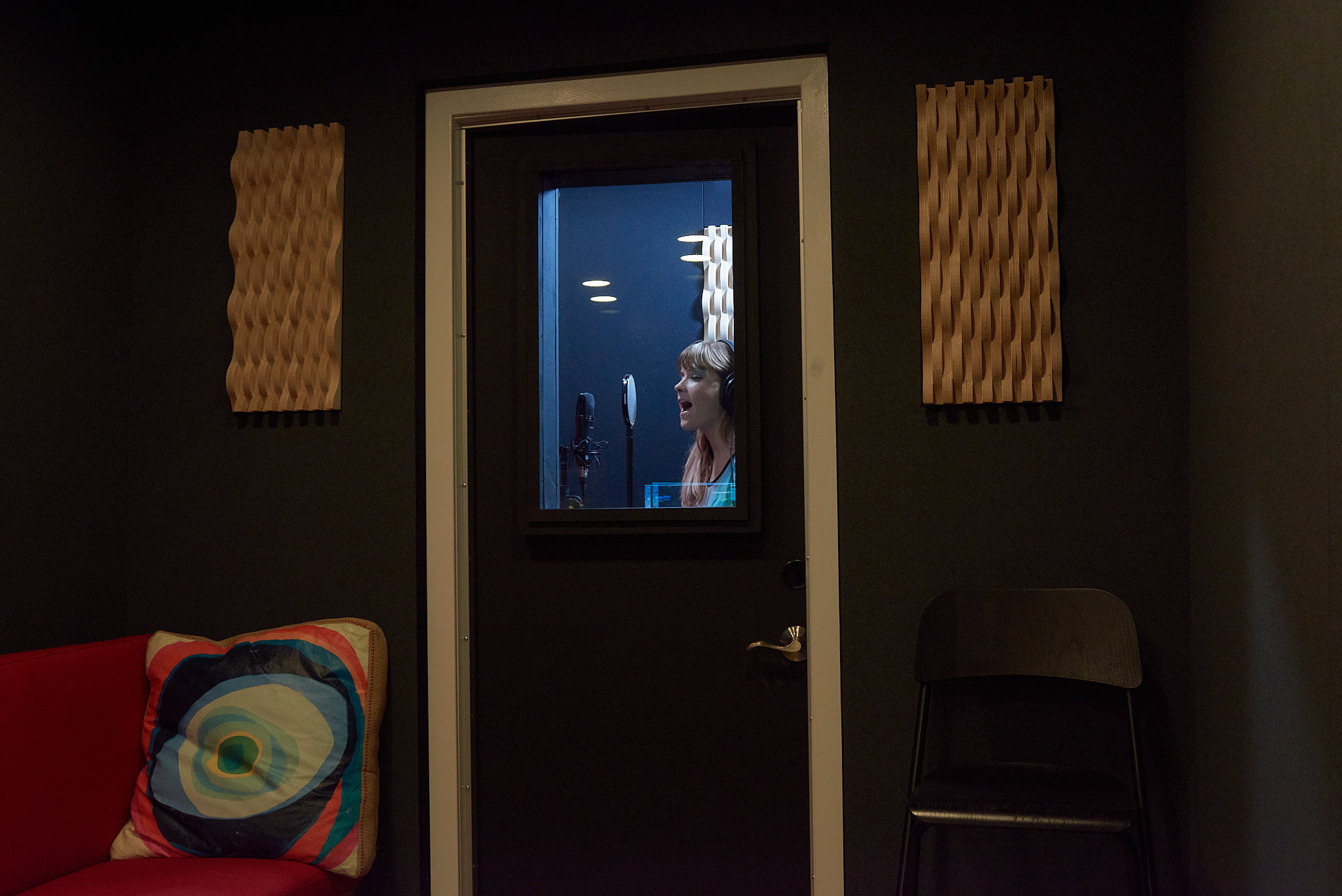 A vocal recording artist singing into a microphone in the booth of a mobile sound studio trailer.